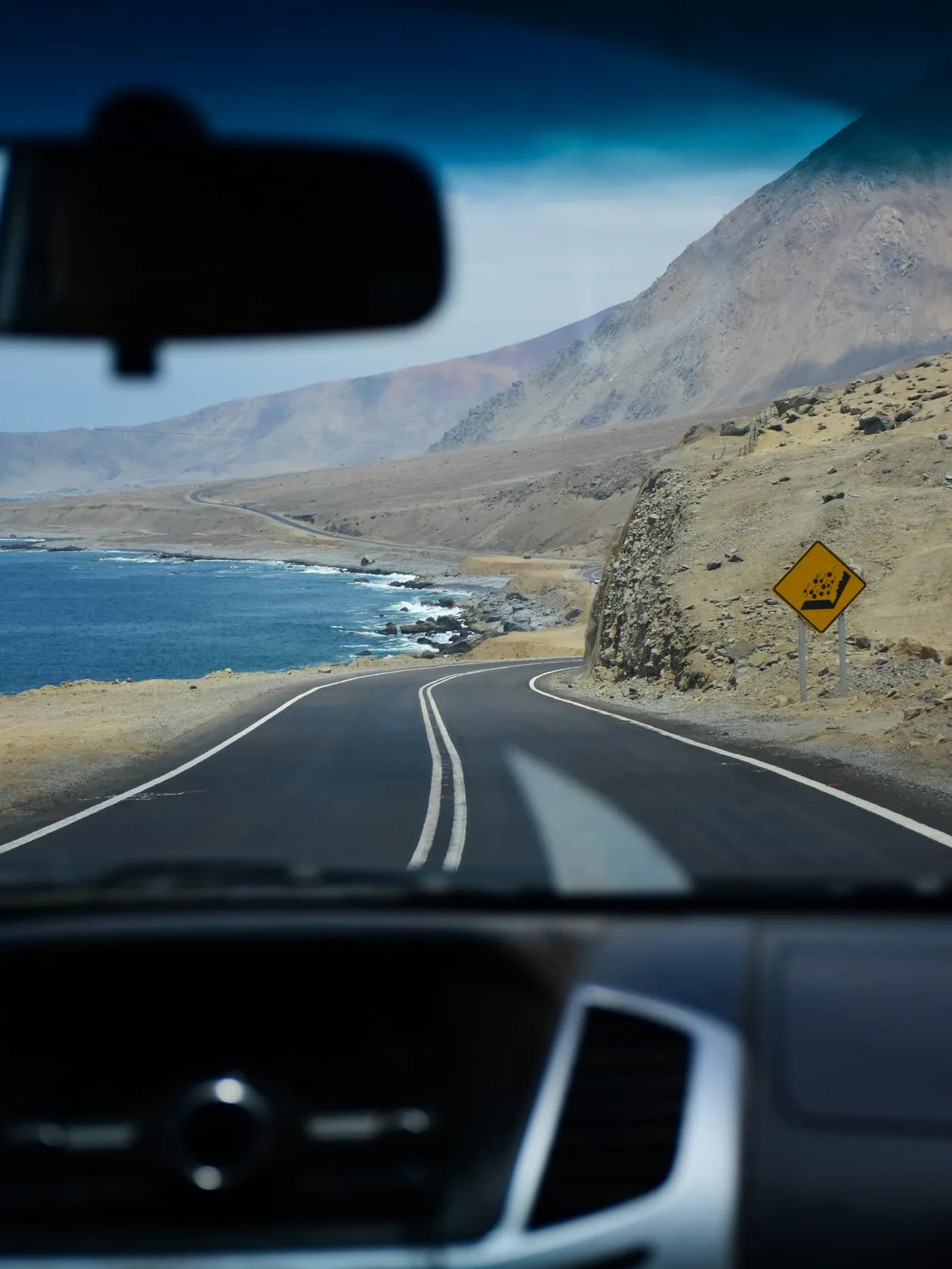 A coastal road curving past the sea, seen through a car's windshield