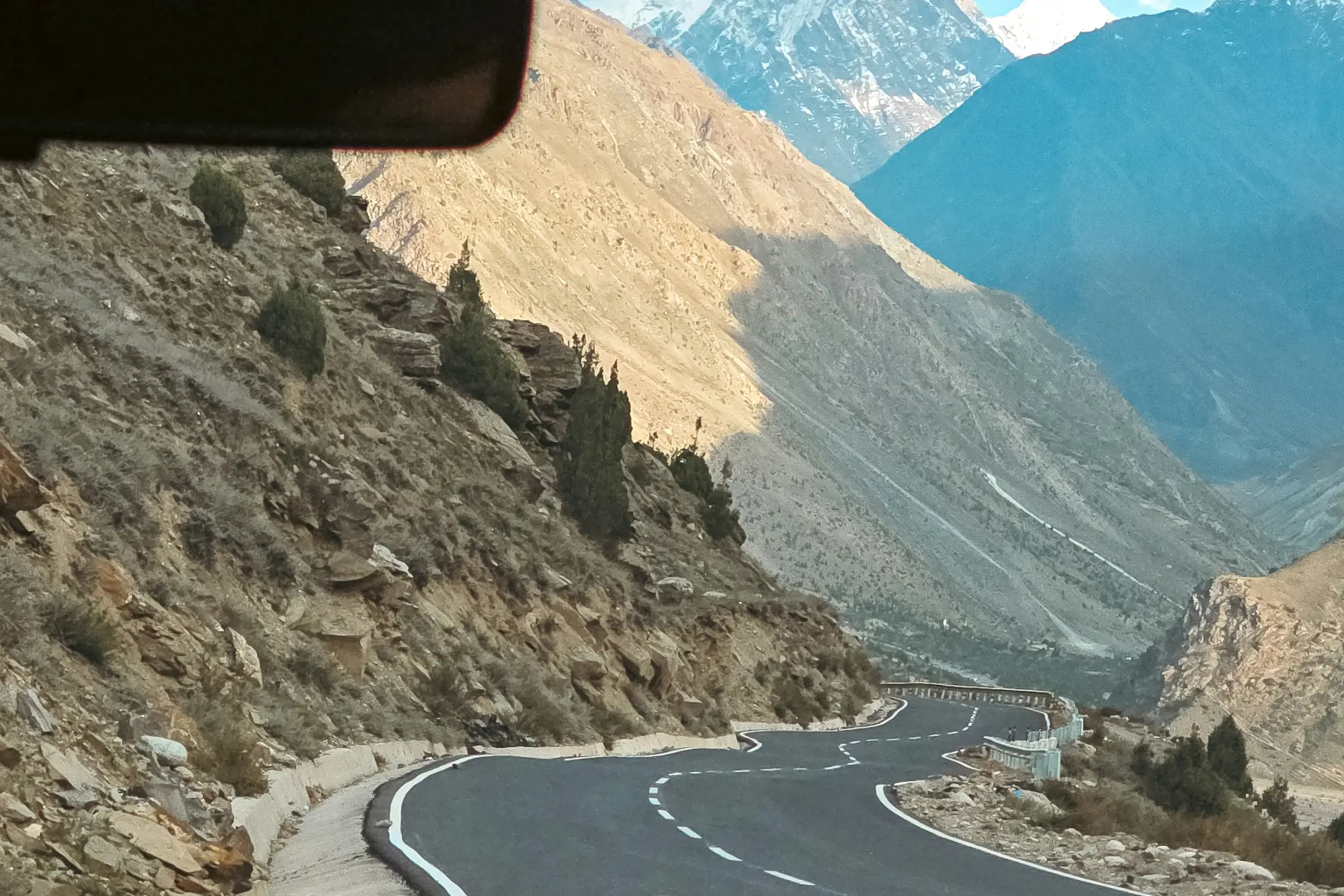 A road winding down a mountain pass toward snowy peaks