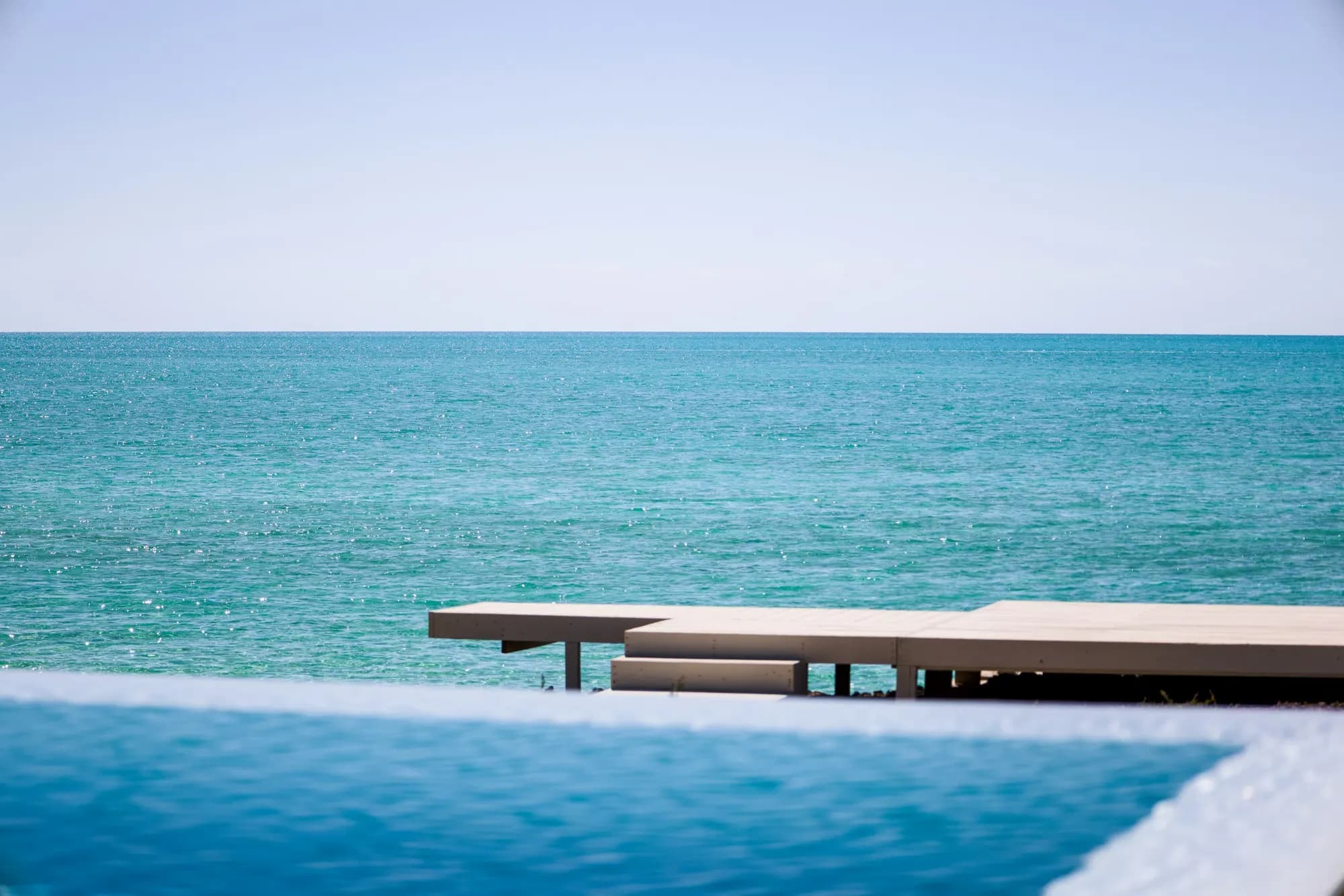 An infinity pool and wooden deck meeting a turquoise sea