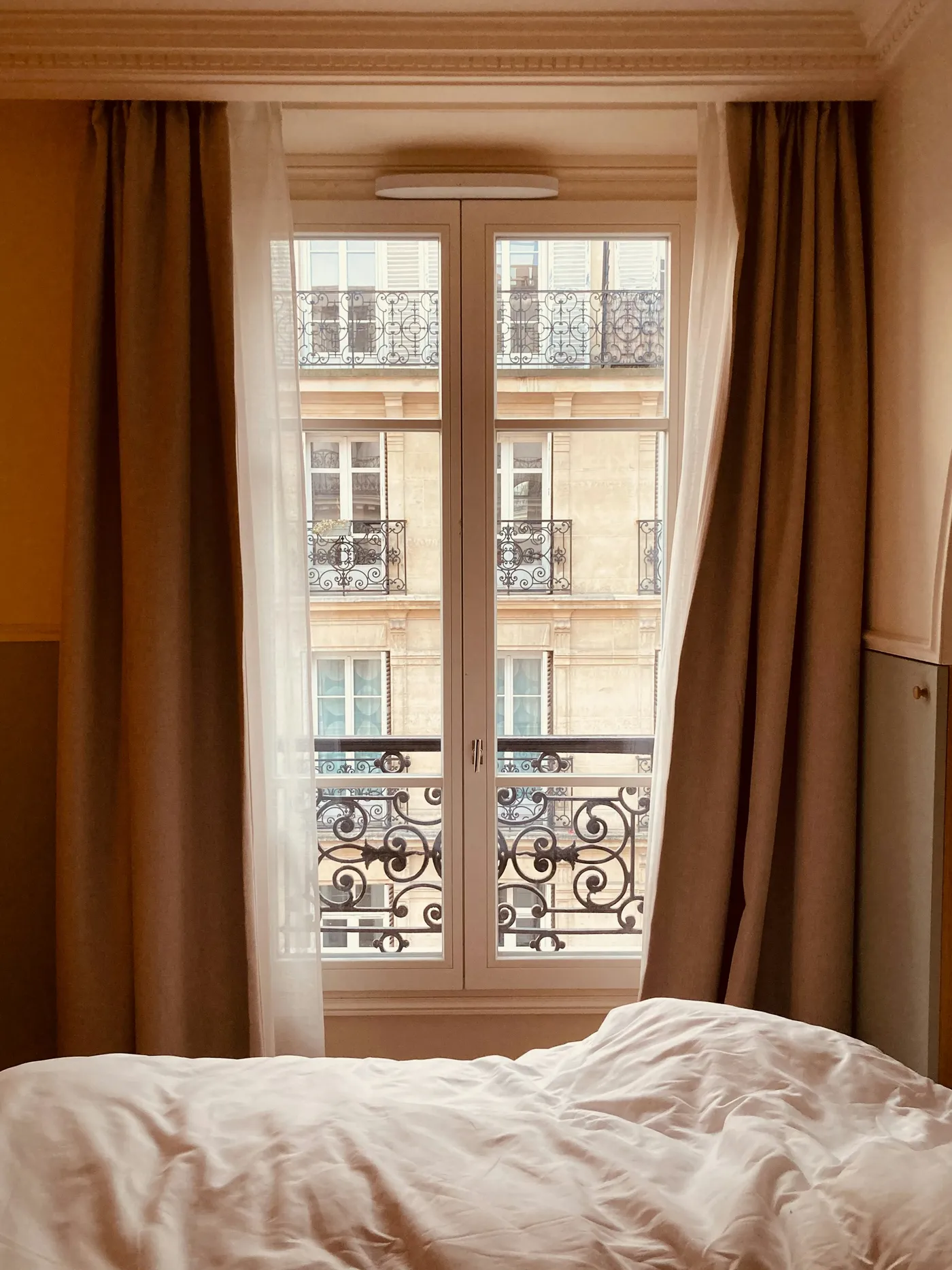 A hotel room in Paris, the bed by tall windows onto a wrought-iron balcony